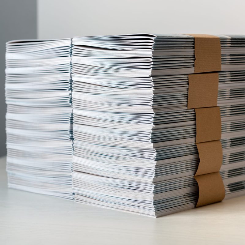 Bundles of newly printed catalogues fastened with brown paper arranged neatly in a stack on a white table
